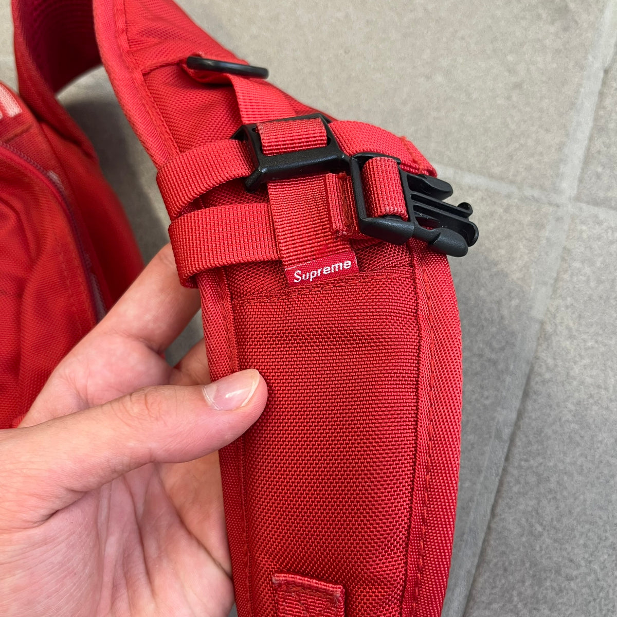 Supreme SS18 Red Backpack features a red construction with a large main compartment suitable for laptops and other larger devices, along with a front zippered pocket for smaller items. It has dual side mesh pockets and a Supreme Box Logo on the front.
