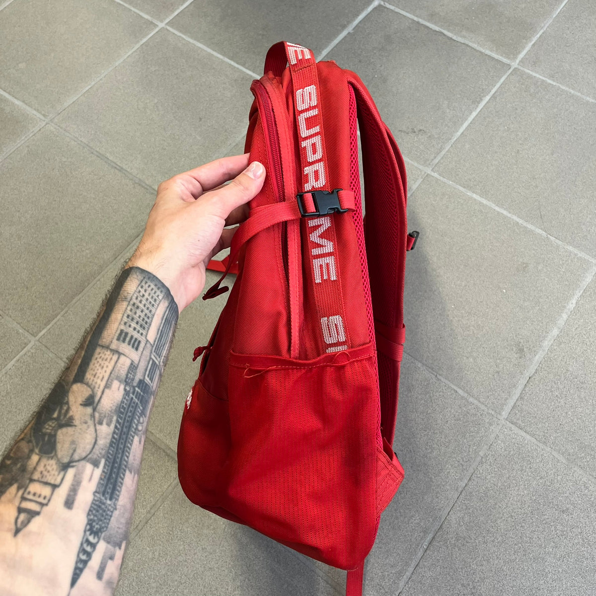 Supreme SS18 Red Backpack features a red construction with a large main compartment suitable for laptops and other larger devices, along with a front zippered pocket for smaller items. It has dual side mesh pockets and a Supreme Box Logo on the front.
