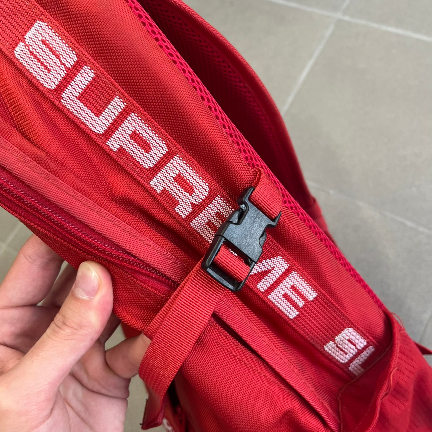 Supreme SS18 Red Backpack features a red construction with a large main compartment suitable for laptops and other larger devices, along with a front zippered pocket for smaller items. It has dual side mesh pockets and a Supreme Box Logo on the front.
