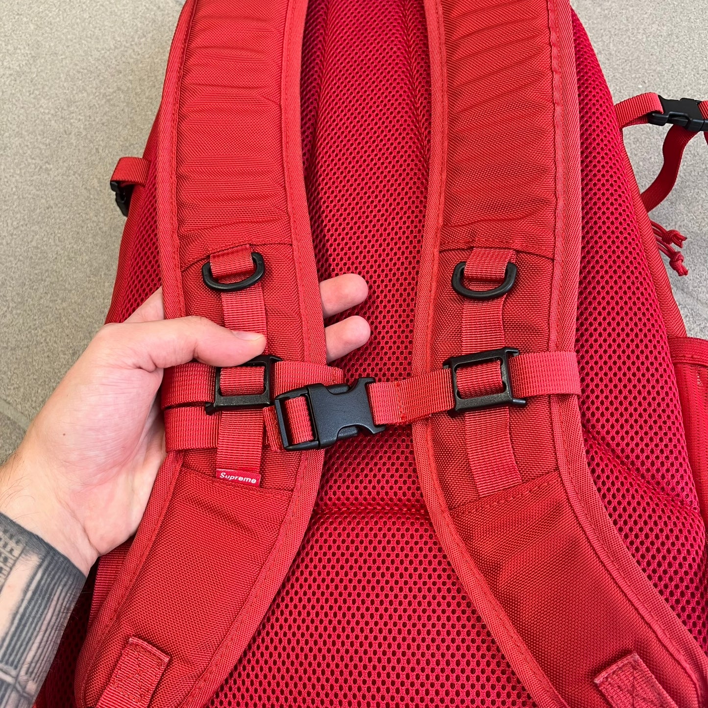 Supreme SS18 Red Backpack features a red construction with a large main compartment suitable for laptops and other larger devices, along with a front zippered pocket for smaller items. It has dual side mesh pockets and a Supreme Box Logo on the front.
