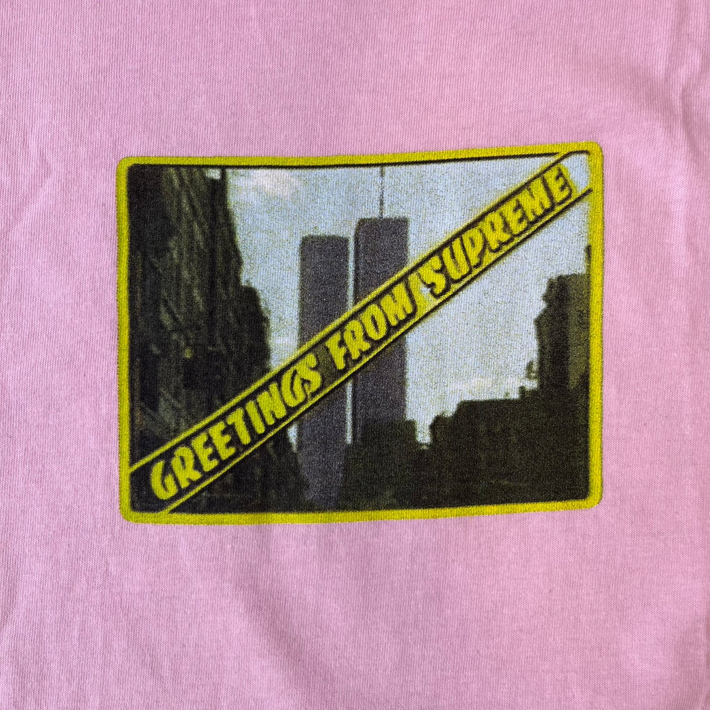 Supreme SS19 Greetings Pink Tee features a pink T-shirt with a front graphic designed as a greeting card showing the New York City skyline. The graphic includes the text “Greetings From Supreme” and depicts the original skyline with the Twin Towers. Released as part of Supreme’s Spring/Summer 2019 collection. Made in USA, 100% Cotton.

