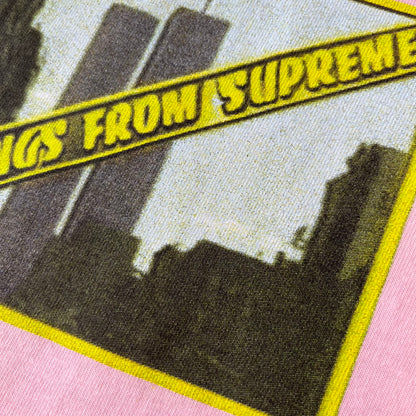 Supreme SS19 Greetings Pink Tee features a pink T-shirt with a front graphic designed as a greeting card showing the New York City skyline. The graphic includes the text “Greetings From Supreme” and depicts the original skyline with the Twin Towers. Released as part of Supreme’s Spring/Summer 2019 collection. Made in USA, 100% Cotton.
