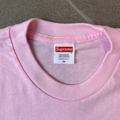 Supreme SS19 Greetings Pink Tee features a pink T-shirt with a front graphic designed as a greeting card showing the New York City skyline. The graphic includes the text “Greetings From Supreme” and depicts the original skyline with the Twin Towers. Released as part of Supreme’s Spring/Summer 2019 collection. Made in USA, 100% Cotton.
