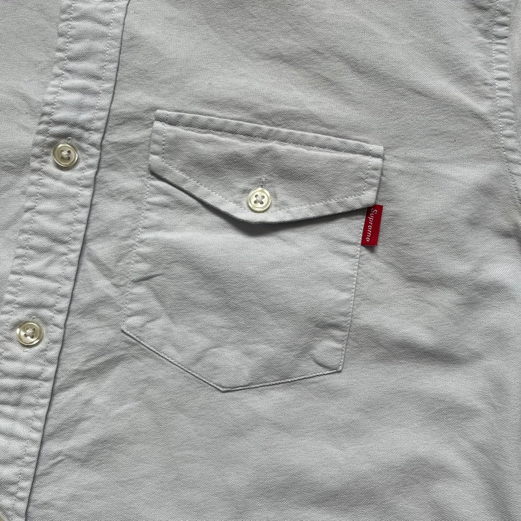 Supreme SS19 Oxford Shirt is a light blue button-up shirt from the Spring/Summer 2019 collection, released on February 21, 2019. It features a button-front closure, a standard collar, and a single chest pocket with a small Supreme tag attached to the side.