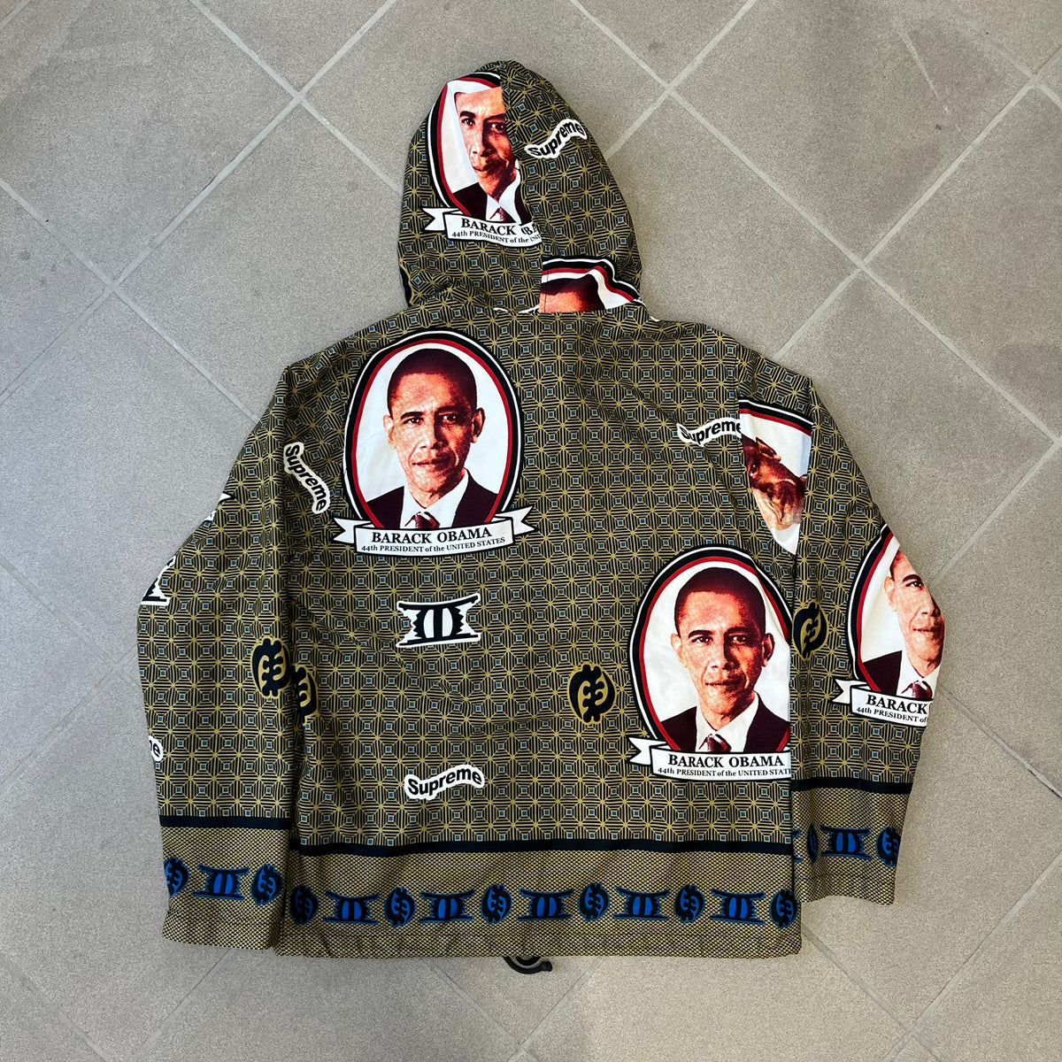 Supreme SS2017 Obama Green Anorak is a green/olive 100% cotton quarter-zip anorak with an all-over patchwork print incorporating Barack Obama’s face, the words “Barack Obama,” and scattered Supreme logos. The design pays homage to the “khanas,” vibrant patterned garments with political graphics made by local designers in Ghana to commemorate the former president’s 2009 visit. It has a drawstring hood and hem and lower front hand pockets.