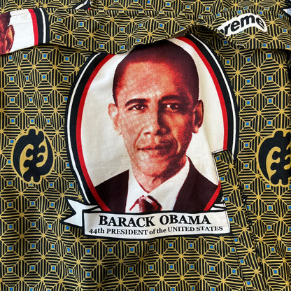 Supreme SS2017 Obama Green Anorak is a green/olive 100% cotton quarter-zip anorak with an all-over patchwork print incorporating Barack Obama’s face, the words “Barack Obama,” and scattered Supreme logos. The design pays homage to the “khanas,” vibrant patterned garments with political graphics made by local designers in Ghana to commemorate the former president’s 2009 visit. It has a drawstring hood and hem and lower front hand pockets.