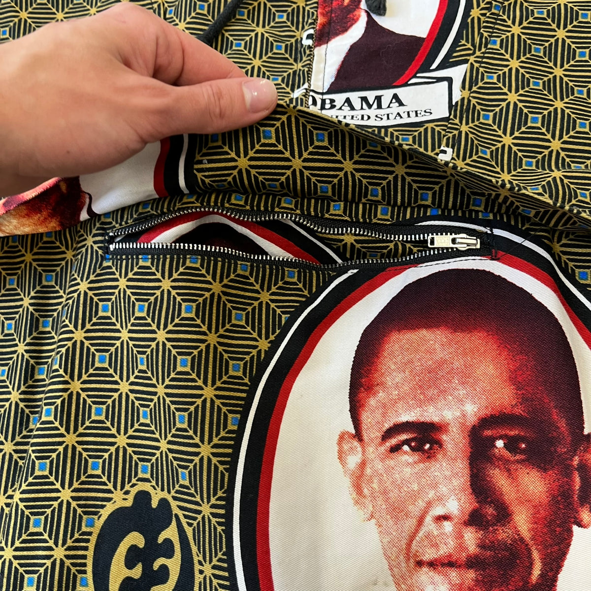 Supreme SS2017 Obama Green Anorak is a green/olive 100% cotton quarter-zip anorak with an all-over patchwork print incorporating Barack Obama’s face, the words “Barack Obama,” and scattered Supreme logos. The design pays homage to the “khanas,” vibrant patterned garments with political graphics made by local designers in Ghana to commemorate the former president’s 2009 visit. It has a drawstring hood and hem and lower front hand pockets.