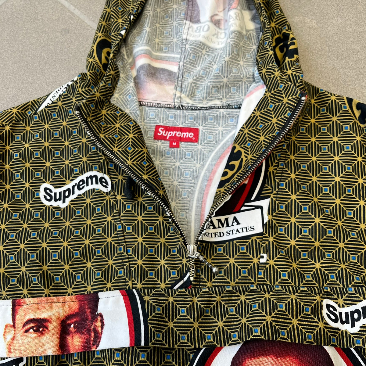 Supreme SS2017 Obama Green Anorak is a green/olive 100% cotton quarter-zip anorak with an all-over patchwork print incorporating Barack Obama’s face, the words “Barack Obama,” and scattered Supreme logos. The design pays homage to the “khanas,” vibrant patterned garments with political graphics made by local designers in Ghana to commemorate the former president’s 2009 visit. It has a drawstring hood and hem and lower front hand pockets.