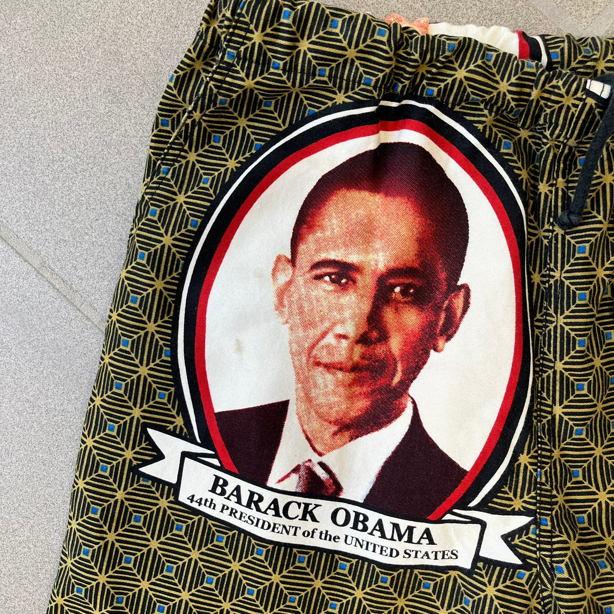 Supreme SS2017 Obama Green Pants are green/olive pants with the all-over patchwork print incorporating Barack Obama’s face, the words “Barack Obama,” and scattered Supreme logos. The design pays homage to the “khanas,” vibrant patterned garments with political graphics made by local designers in Ghana to commemorate the former president’s 2009 visit. They have two front pockets and one back pocket.
