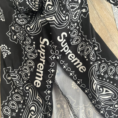 Supreme SS26 Ghostface Mask is a PVC face mask released on April 30, 2026, as part of the Spring/Summer 2026 collection. The mask features the classic white Ghostface design, combined with a black fabric hood element covered in white bandana-style patterns and integrated Supreme tags. Additional hanging strips on the sides enhance the hooded visual effect.