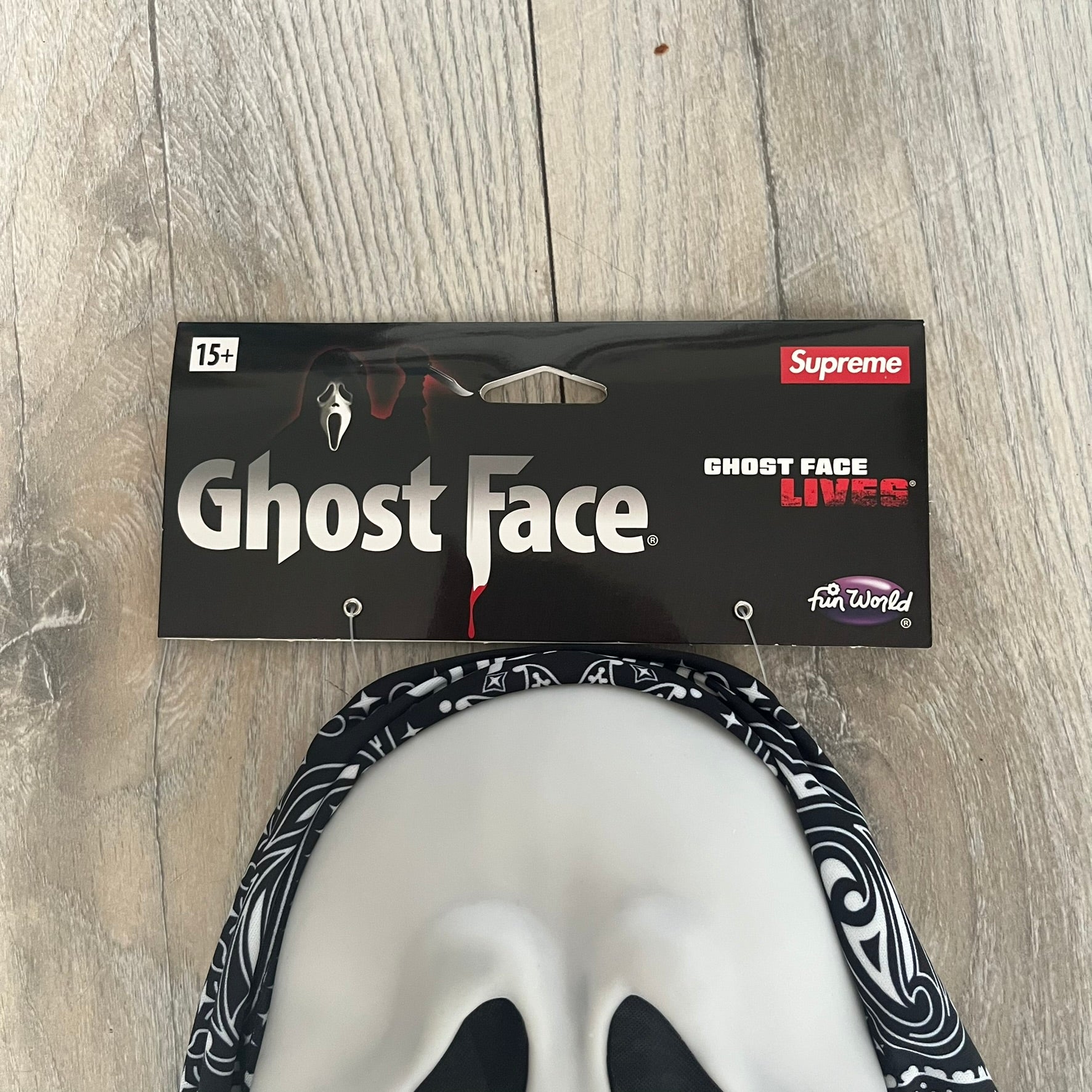 Supreme SS26 Ghostface Mask is a PVC face mask released on April 30, 2026, as part of the Spring/Summer 2026 collection. The mask features the classic white Ghostface design, combined with a black fabric hood element covered in white bandana-style patterns and integrated Supreme tags. Additional hanging strips on the sides enhance the hooded visual effect.