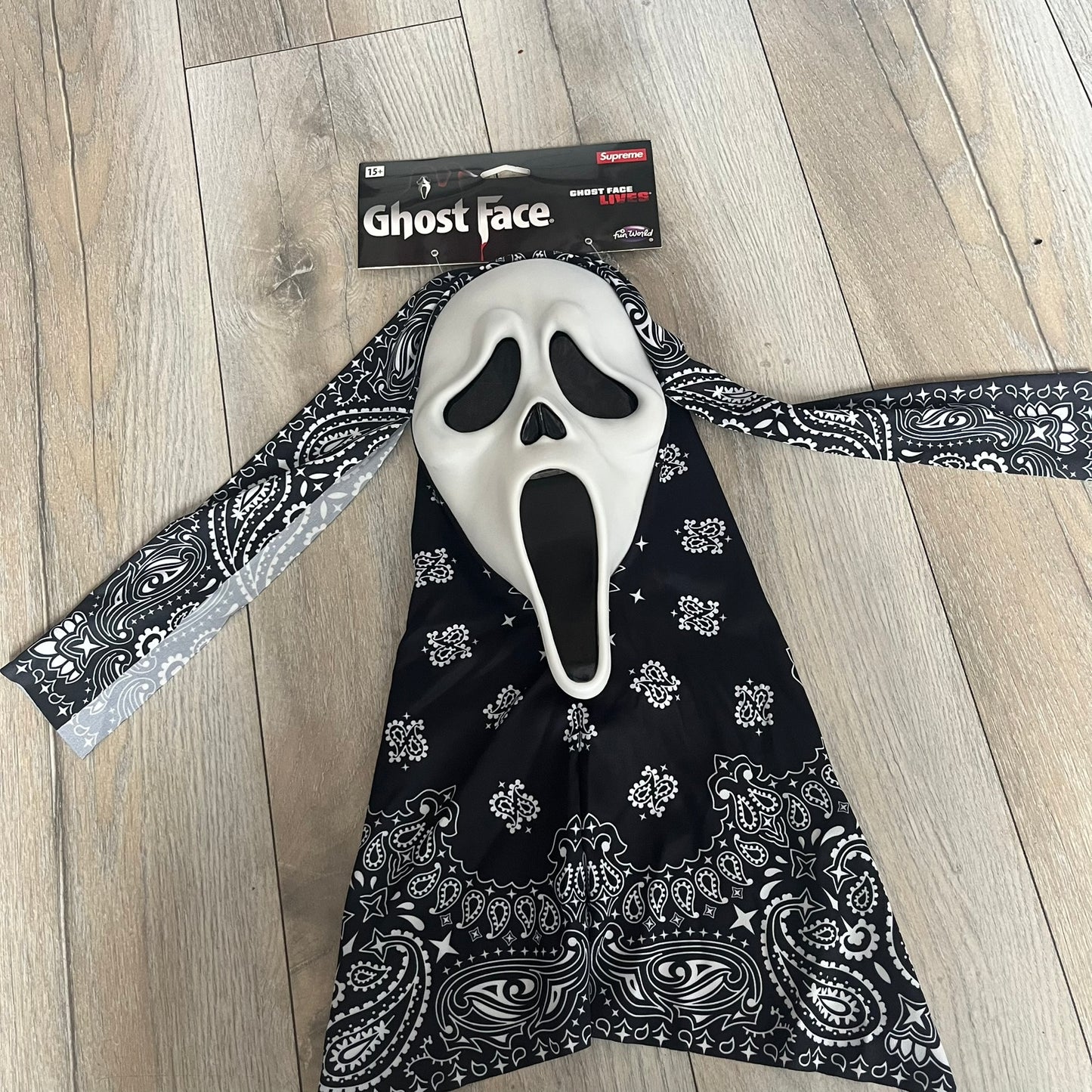 Supreme SS26 Ghostface Mask is a PVC face mask released on April 30, 2026, as part of the Spring/Summer 2026 collection. The mask features the classic white Ghostface design, combined with a black fabric hood element covered in white bandana-style patterns and integrated Supreme tags. Additional hanging strips on the sides enhance the hooded visual effect.