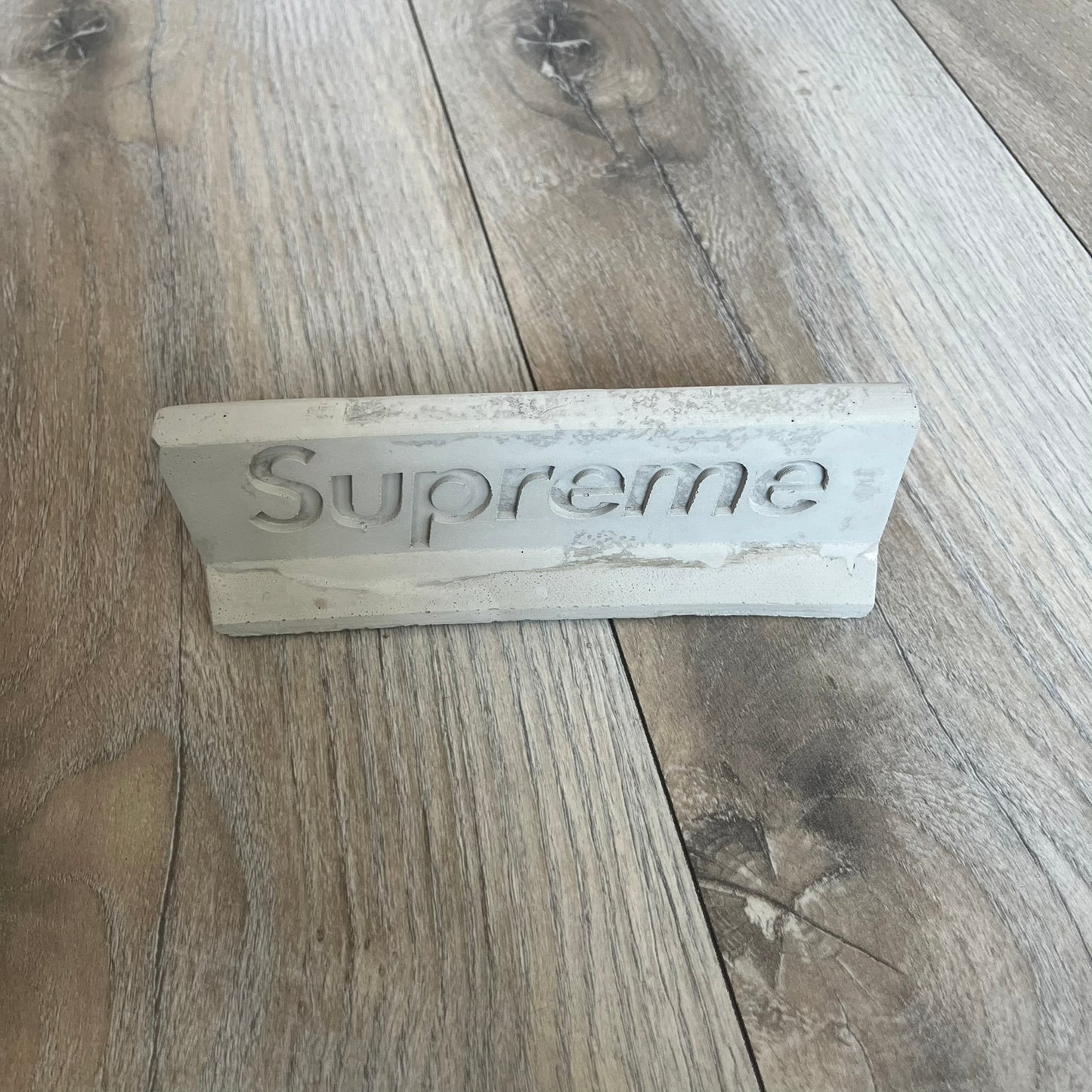 Supreme SS26 Mini Materials 1:12 Scale Jersey Barrier is a grey miniature accessory released on March 26, 2026, as part of the Spring/Summer 2026 collection. The piece replicates a standard jersey barrier in 1:12 scale with realistic construction-style detailing. This item was produced as part of Supreme’s Mini Materials accessory line.