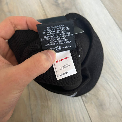 Supreme SS26 New Era Ghostface Black Beanie is a black knit beanie released on March 26, 2026, as part of the Spring/Summer 2026 collection. The front features a white Ghostface graphic, while the back includes “Supreme” text in a gothic-style font, with a small New Era logo embroidered on the side. The beanie is constructed from knit fabric for warmth and everyday wear.