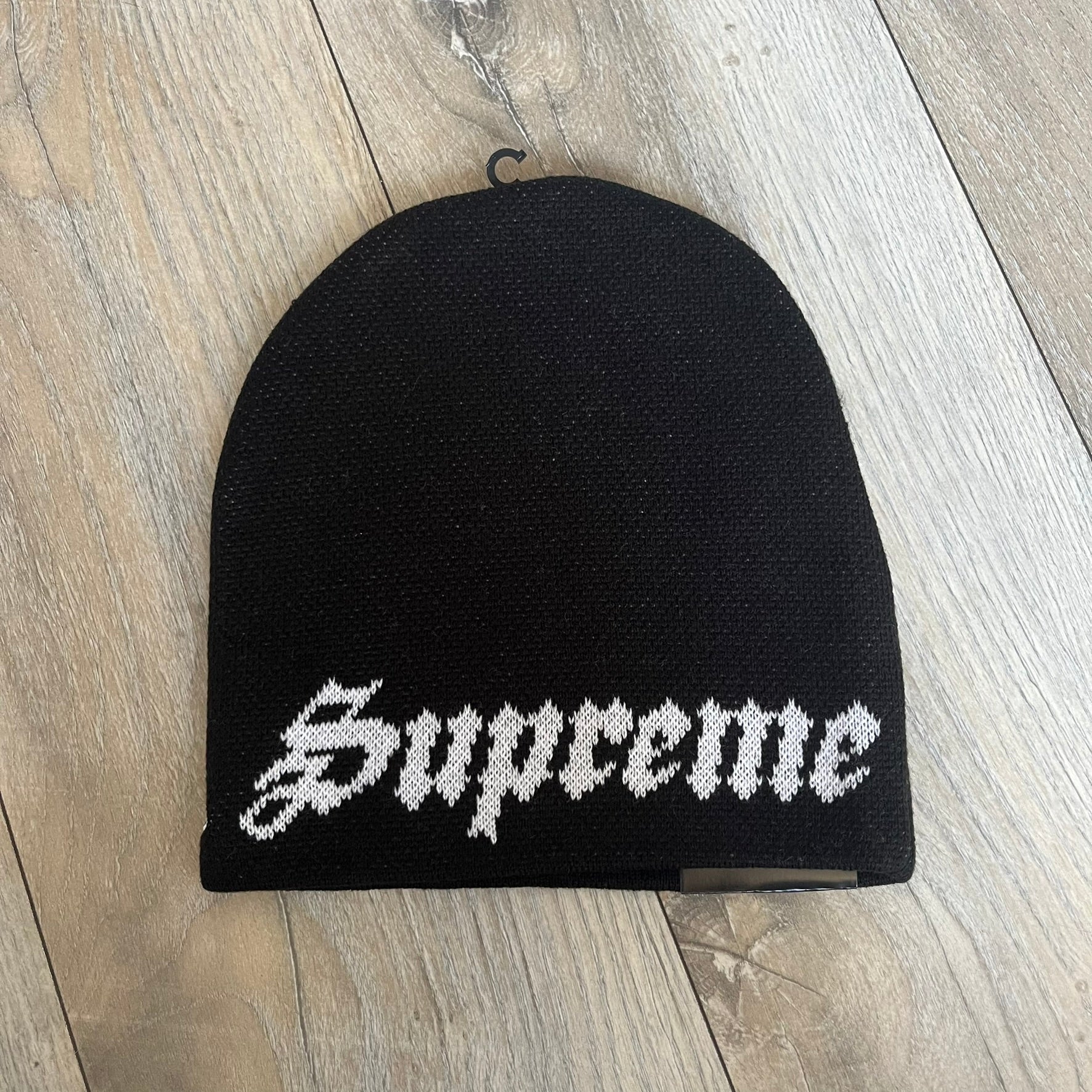 Supreme SS26 New Era Ghostface Black Beanie is a black knit beanie released on March 26, 2026, as part of the Spring/Summer 2026 collection. The front features a white Ghostface graphic, while the back includes “Supreme” text in a gothic-style font, with a small New Era logo embroidered on the side. The beanie is constructed from knit fabric for warmth and everyday wear.