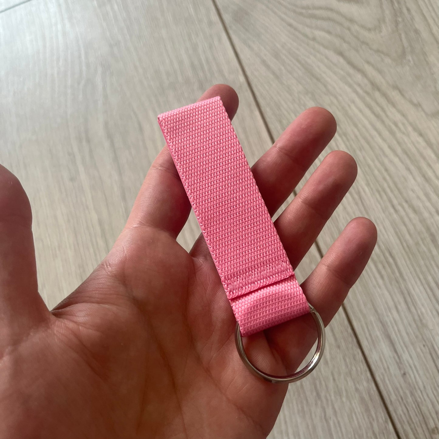  Supreme SS26 Webbing Keychain is a pink keychain from the Spring/Summer 2026 collection. It features a silver-tone 1-inch keyring and a pink rubber Supreme box logo patch attached to the front. The reverse side is plain with no additional graphics.