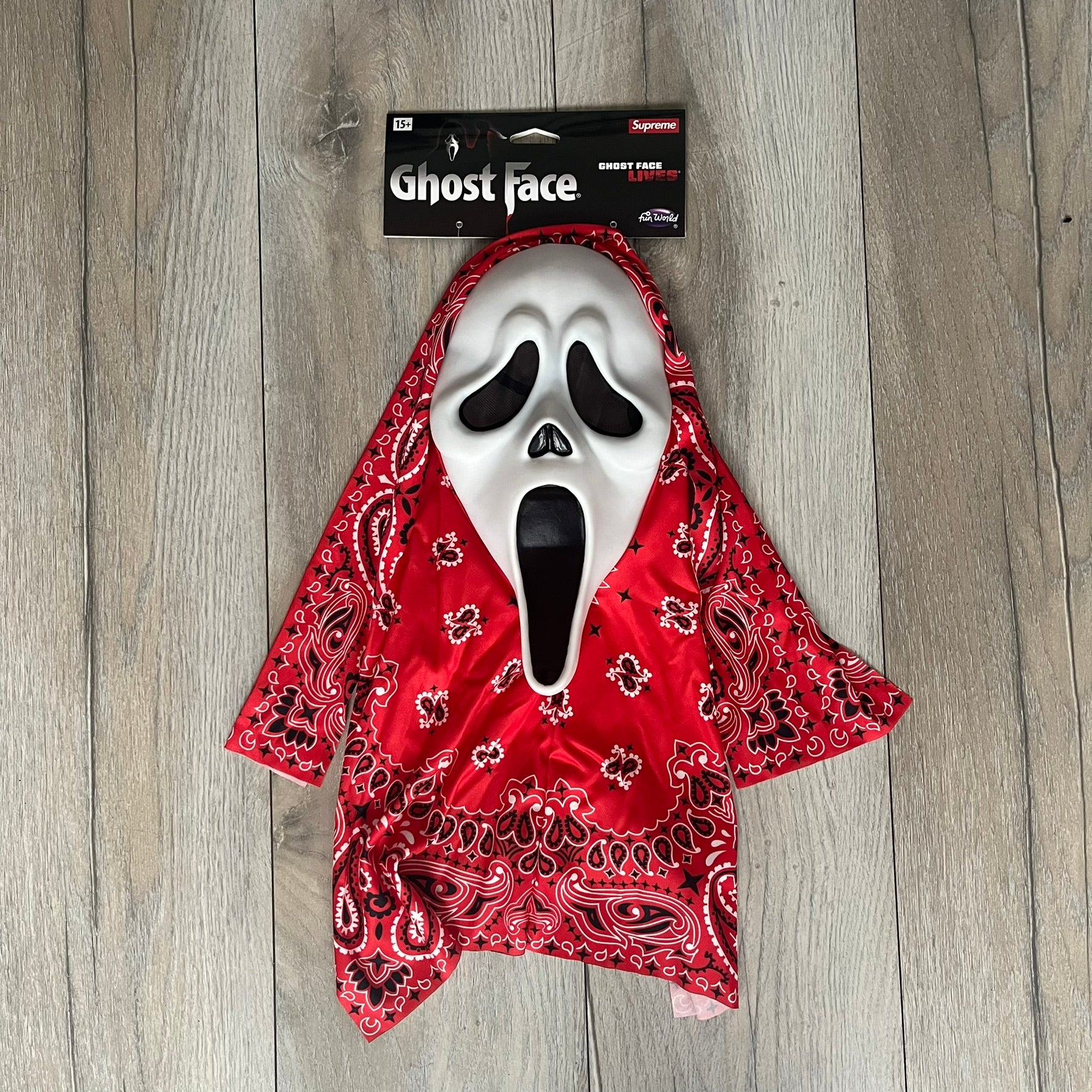 Supreme SS26 Ghostface Mask is a PVC face mask released on April 30, 2026, as part of the Spring/Summer 2026 collection. The mask features the classic white Ghostface design, combined with a red fabric hood element covered in white and black bandana-style patterns and integrated Supreme tags. Additional hanging strips on the sides enhance the hooded visual effect.