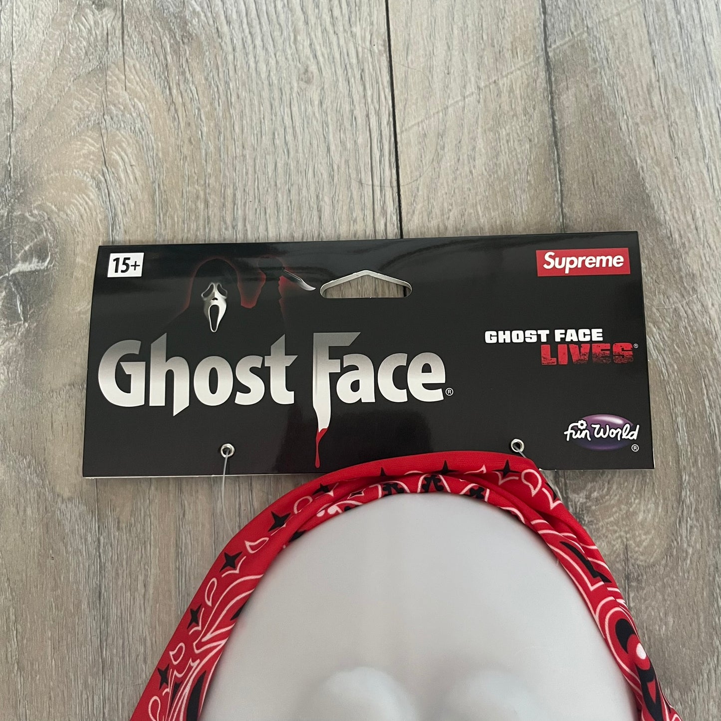 Supreme SS26 Ghostface Mask is a PVC face mask released on April 30, 2026, as part of the Spring/Summer 2026 collection. The mask features the classic white Ghostface design, combined with a red fabric hood element covered in white and black bandana-style patterns and integrated Supreme tags. Additional hanging strips on the sides enhance the hooded visual effect.