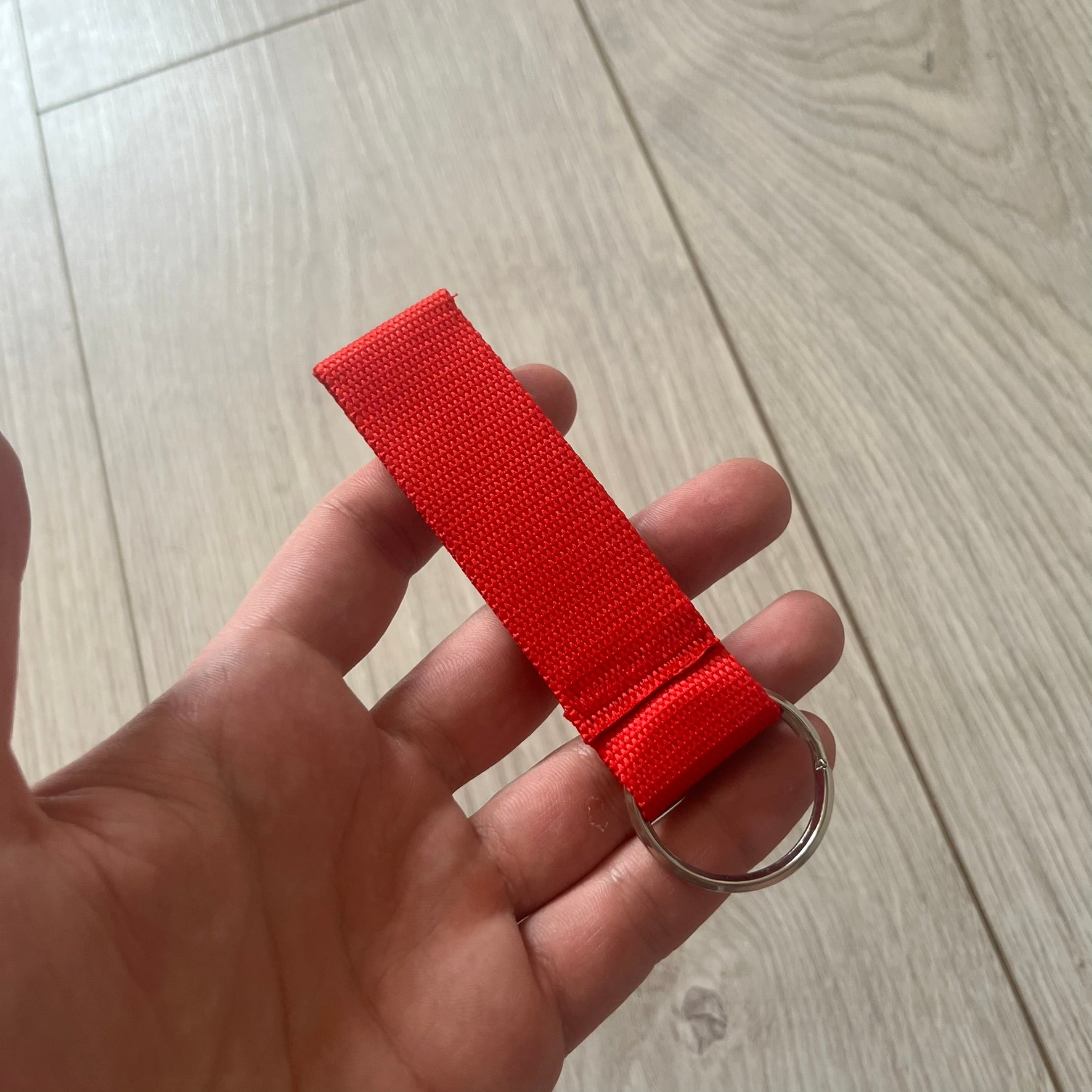 Supreme SS26 Webbing Keychain is a red keychain from the Spring/Summer 2026 collection. It features a silver-tone 1-inch keyring and a red rubber Supreme box logo patch attached to the front. The reverse side is plain with no additional graphics.