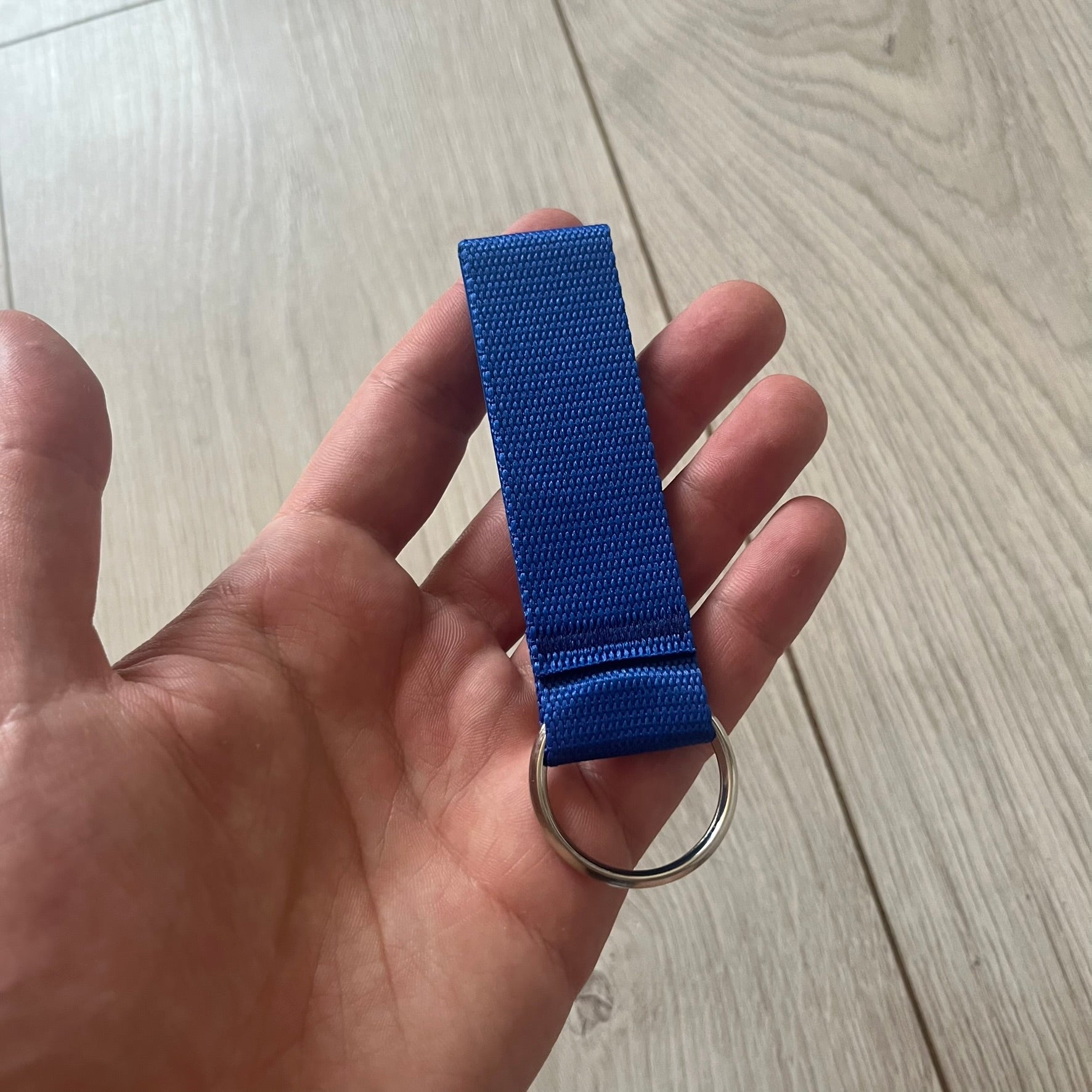 Supreme SS26 Webbing Keychain is a blue keychain from the Spring/Summer 2026 collection. It features a silver-tone 1-inch keyring and a blue rubber Supreme box logo patch attached to the front. The reverse side is plain with no additional graphics.