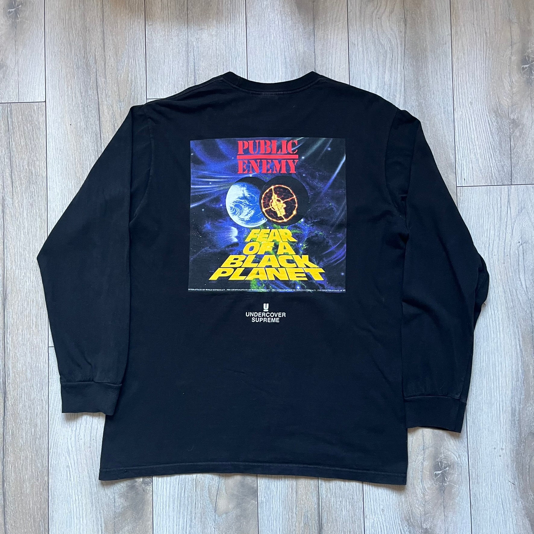 Supreme Undercover Public Enemy Counterattack SS18 Longsleeve Tee is a black long-sleeve T-shirt released on March 15, 2018, crafted from 100% cotton. The front features white “The Counterattack On World Supremacy” text with a small Supreme UNDERCOVER logo beneath, while the back displays a large Public Enemy “Fear of a Black Planet” graphic with galaxy and planet imagery and the same co-branded logo below. The design includes a ribbed crewneck and ribbed cuffs, reflecting the SS18 collaboration between Sup