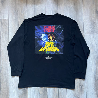 Supreme Undercover Public Enemy Counterattack SS18 Longsleeve Tee is a black long-sleeve T-shirt released on March 15, 2018, crafted from 100% cotton. The front features white “The Counterattack On World Supremacy” text with a small Supreme UNDERCOVER logo beneath, while the back displays a large Public Enemy “Fear of a Black Planet” graphic with galaxy and planet imagery and the same co-branded logo below. The design includes a ribbed crewneck and ribbed cuffs, reflecting the SS18 collaboration between Sup