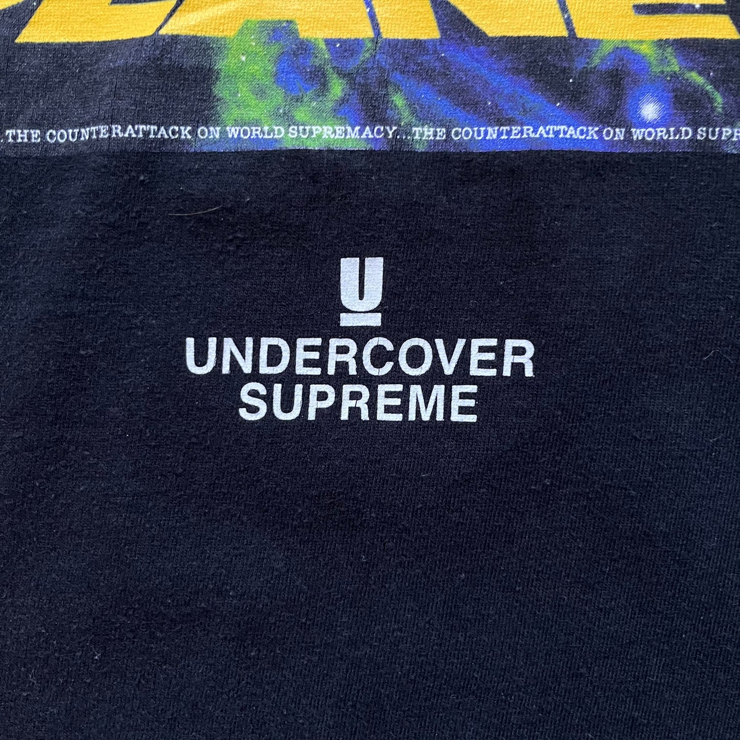 Supreme Undercover Public Enemy Counterattack SS18 Longsleeve Tee is a black long-sleeve T-shirt released on March 15, 2018, crafted from 100% cotton. The front features white “The Counterattack On World Supremacy” text with a small Supreme UNDERCOVER logo beneath, while the back displays a large Public Enemy “Fear of a Black Planet” graphic with galaxy and planet imagery and the same co-branded logo below. The design includes a ribbed crewneck and ribbed cuffs, reflecting the SS18 collaboration between Sup