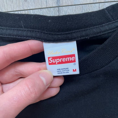 Supreme Undercover Public Enemy Counterattack SS18 Longsleeve Tee is a black long-sleeve T-shirt released on March 15, 2018, crafted from 100% cotton. The front features white “The Counterattack On World Supremacy” text with a small Supreme UNDERCOVER logo beneath, while the back displays a large Public Enemy “Fear of a Black Planet” graphic with galaxy and planet imagery and the same co-branded logo below. The design includes a ribbed crewneck and ribbed cuffs, reflecting the SS18 collaboration between Sup