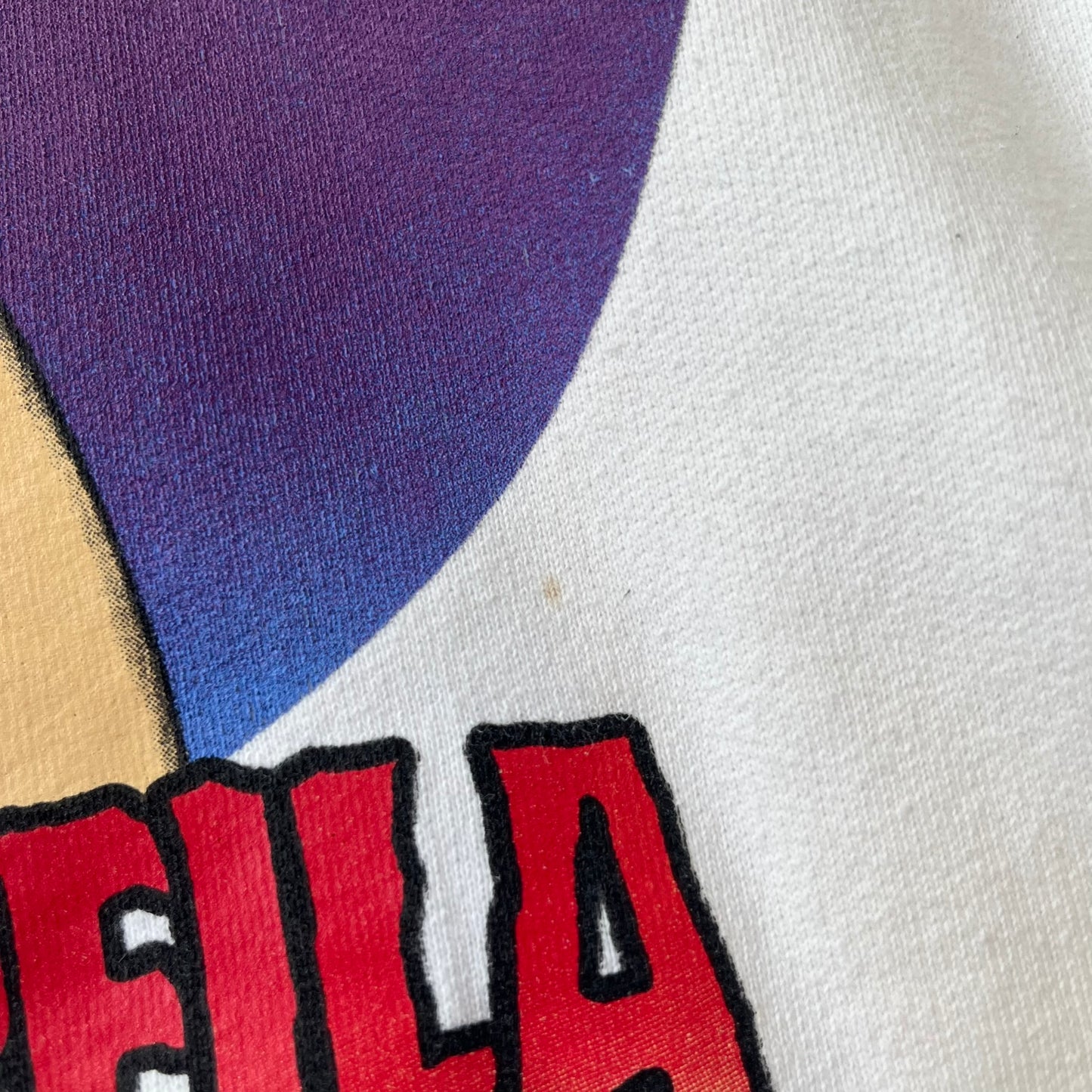 Supreme Vampirella SS17 White Hoodie features a white 100% cotton construction with a front graphic of Vampirella against a purple circular background. A “Vampirella” logo is printed underneath, while black outlined Supreme logos run vertically along the sleeves.
