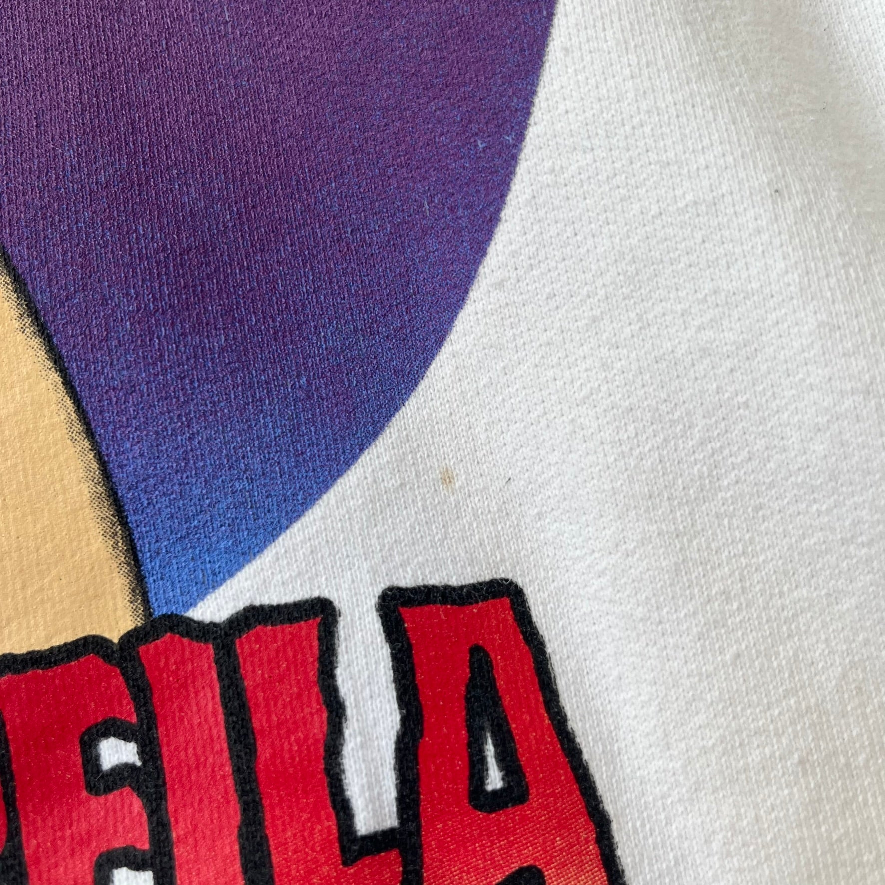 Supreme Vampirella SS17 White Hoodie features a white 100% cotton construction with a front graphic of Vampirella against a purple circular background. A “Vampirella” logo is printed underneath, while black outlined Supreme logos run vertically along the sleeves.
