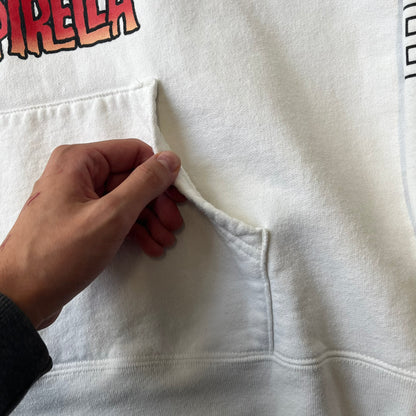 Supreme Vampirella SS17 White Hoodie features a white 100% cotton construction with a front graphic of Vampirella against a purple circular background. A “Vampirella” logo is printed underneath, while black outlined Supreme logos run vertically along the sleeves.
