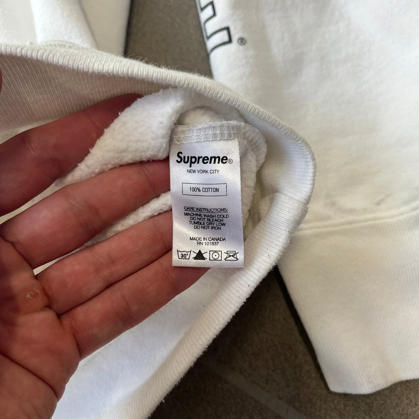 Supreme Vampirella SS17 White Hoodie features a white 100% cotton construction with a front graphic of Vampirella against a purple circular background. A “Vampirella” logo is printed underneath, while black outlined Supreme logos run vertically along the sleeves.
