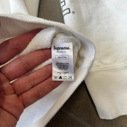 Supreme Vampirella SS17 White Hoodie features a white 100% cotton construction with a front graphic of Vampirella against a purple circular background. A “Vampirella” logo is printed underneath, while black outlined Supreme logos run vertically along the sleeves.
