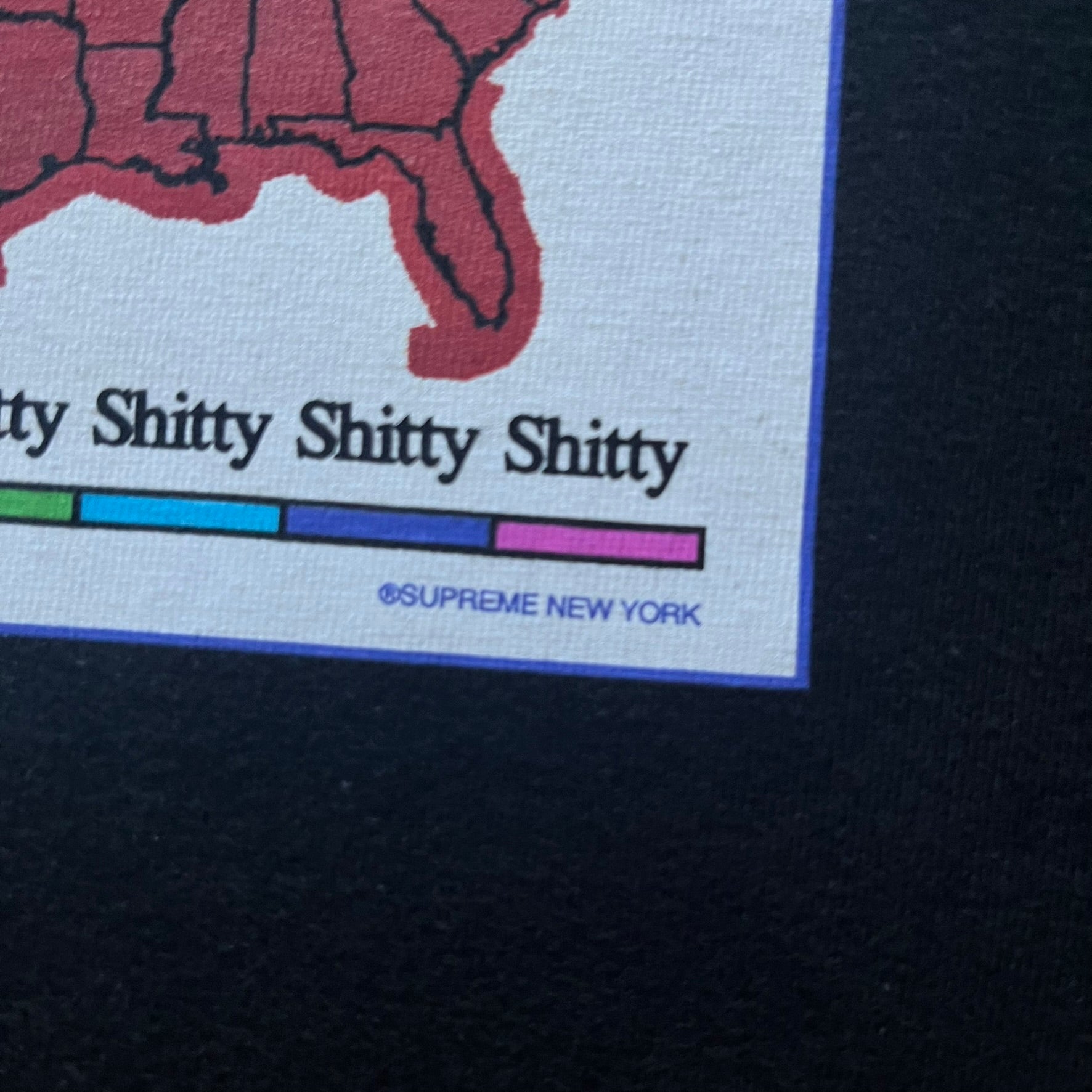 Supreme “Weather” FW23 tee in black, showcasing a satirical weather map graphic of the USA. Below sits a gradient bar in red-to-pink tones, with every category marked “Shitty.” Includes small Supreme New York text detail, true to the collection.