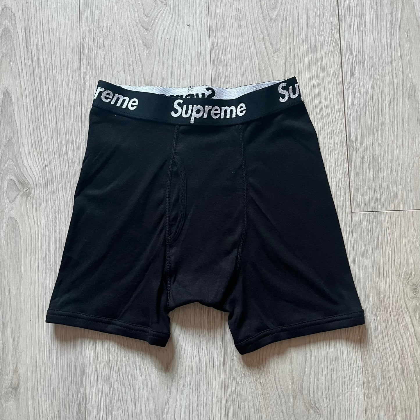 Supreme x Hanes black boxer briefs made of cotton with a stretch fit. Features a black elastic waistband with white Supreme logo text in Futura Oblique font. Classic Hanes base model with co-branded detailing.
