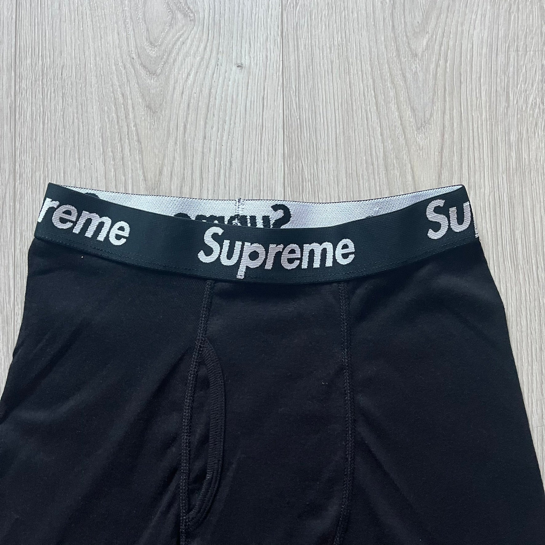 Supreme x Hanes black boxer briefs made of cotton with a stretch fit. Features a black elastic waistband with white Supreme logo text in Futura Oblique font. Classic Hanes base model with co-branded detailing.