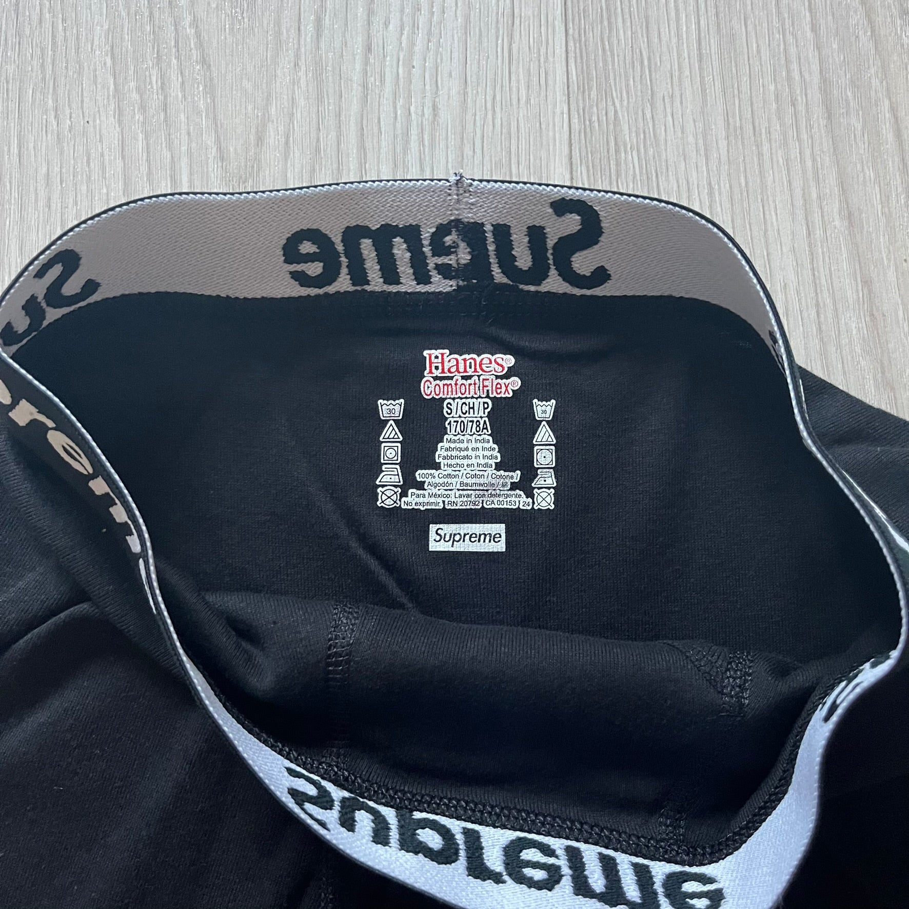 Supreme x Hanes black boxer briefs made of cotton with a stretch fit. Features a black elastic waistband with white Supreme logo text in Futura Oblique font. Classic Hanes base model with co-branded detailing.