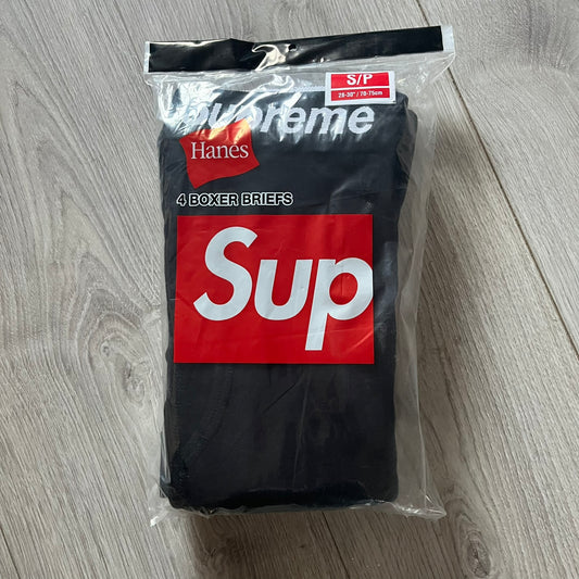 Supreme x Hanes black boxer briefs made of cotton with a stretch fit. Features a black elastic waistband with white Supreme logo text in Futura Oblique font. Classic Hanes base model with co-branded detailing.
