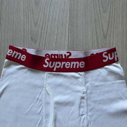 Supreme x Hanes white boxer briefs made of cotton with a stretch fit. Features a red elastic waistband with white Supreme logo text in Futura Oblique font. Classic Hanes base model with co-branded detailing.