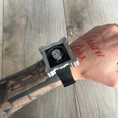 Swatch x Jeremy Scott 2011 Portrait Analog Watch SUOZ121 is an analog watch from the designer’s second collaboration with Swatch, featuring a portrait of Jeremy Scott on the dial and his signature on the strap. The watch includes a silver-tone ornate removable frame, black dial with fixed bezel, and Swiss-made quartz movement. It is water resistant up to 30 meters, comes with original packaging, and retains protective film, with the hour hand partially obscured by the portrait design.