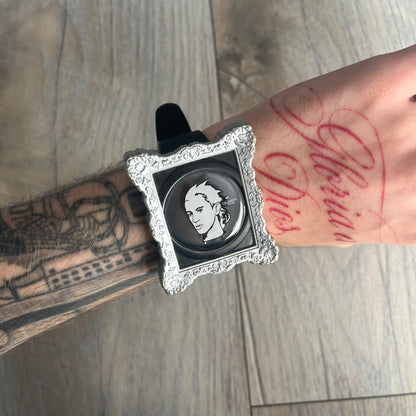 Swatch x Jeremy Scott 2011 Portrait Analog Watch SUOZ121 is an analog watch from the designer’s second collaboration with Swatch, featuring a portrait of Jeremy Scott on the dial and his signature on the strap. The watch includes a silver-tone ornate removable frame, black dial with fixed bezel, and Swiss-made quartz movement. It is water resistant up to 30 meters, comes with original packaging, and retains protective film, with the hour hand partially obscured by the portrait design.