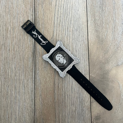 Swatch x Jeremy Scott 2011 Portrait Analog Watch SUOZ121 is an analog watch from the designer’s second collaboration with Swatch, featuring a portrait of Jeremy Scott on the dial and his signature on the strap. The watch includes a silver-tone ornate removable frame, black dial with fixed bezel, and Swiss-made quartz movement. It is water resistant up to 30 meters, comes with original packaging, and retains protective film, with the hour hand partially obscured by the portrait design.