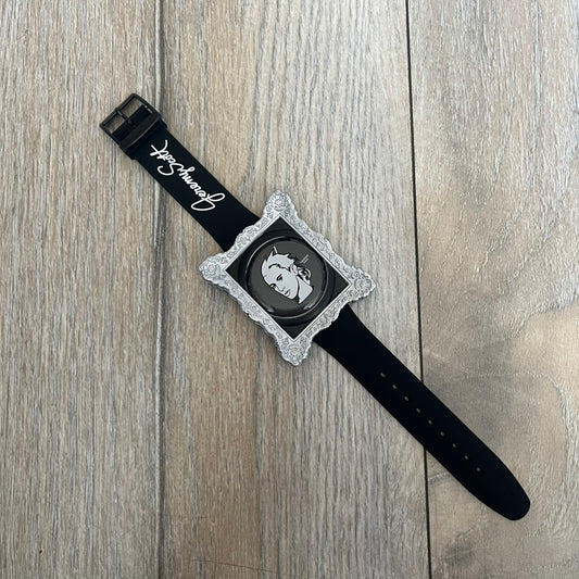 Swatch x Jeremy Scott 2011 Portrait Analog Watch SUOZ121 is an analog watch from the designer’s second collaboration with Swatch, featuring a portrait of Jeremy Scott on the dial and his signature on the strap. The watch includes a silver-tone ornate removable frame, black dial with fixed bezel, and Swiss-made quartz movement. It is water resistant up to 30 meters, comes with original packaging, and retains protective film, with the hour hand partially obscured by the portrait design.