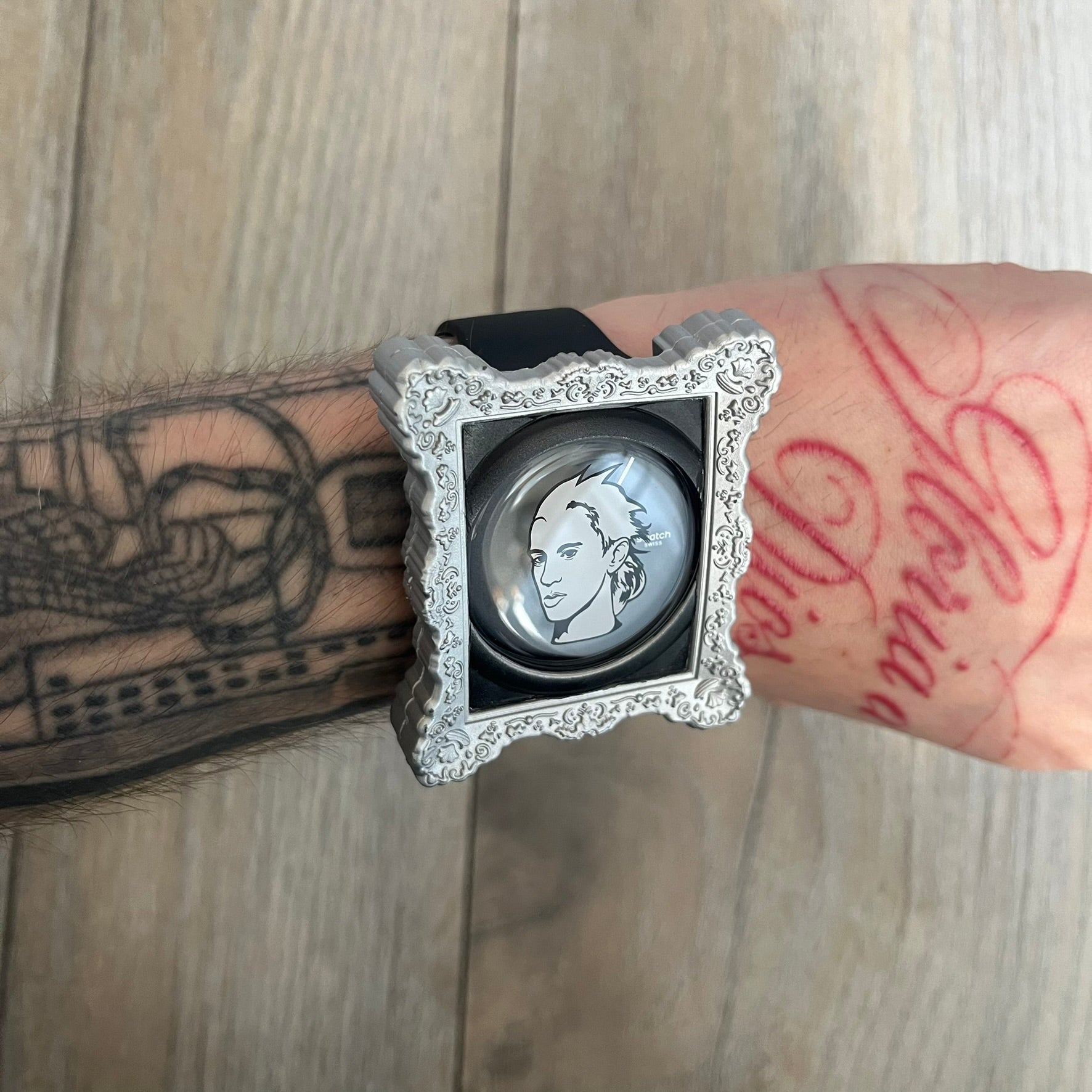 Swatch x Jeremy Scott 2011 Portrait Analog Watch SUOZ121 is an analog watch from the designer’s second collaboration with Swatch, featuring a portrait of Jeremy Scott on the dial and his signature on the strap. The watch includes a silver-tone ornate removable frame, black dial with fixed bezel, and Swiss-made quartz movement. It is water resistant up to 30 meters, comes with original packaging, and retains protective film, with the hour hand partially obscured by the portrait design.