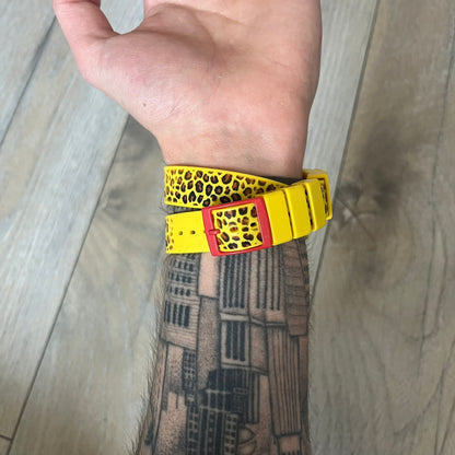 Swatch x Jeremy Scott 2011 Punk Analog Watch GZ251 is a quartz watch from the Gent Original line featuring a bright green dial with black hands and a plastic case. The design includes a comically long silicone strap with leopard print that wraps twice around the wrist, secured with multiple yellow loops, and Jeremy Scott branding on the upper strap. The watch is water resistant to 3 bar and comes with original box and papers.