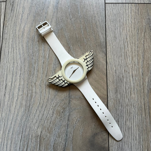 Swatch x Jeremy Scott SUOZ103 “Wings” analog watch released in 2011 as part of Jeremy Scott’s collaboration with Swatch. The watch features a 41 mm case, white dial with Swatch text, black hands, and a white silicone strap. The design includes removable clip-on white 3D wings with black detailing, Swiss quartz movement, patented Swatch battery system, water resistance, and Jeremy Scott branding on the caseback.