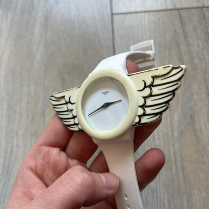 Swatch x Jeremy Scott SUOZ103 “Wings” analog watch released in 2011 as part of Jeremy Scott’s collaboration with Swatch. The watch features a 41 mm case, white dial with Swatch text, black hands, and a white silicone strap. The design includes removable clip-on white 3D wings with black detailing, Swiss quartz movement, patented Swatch battery system, water resistance, and Jeremy Scott branding on the caseback.