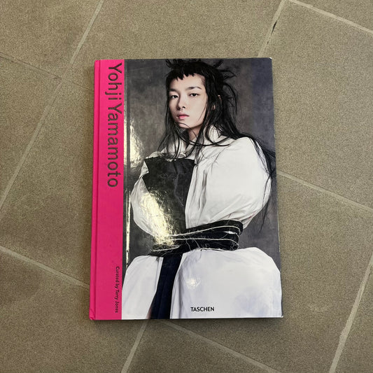 Taschen *Yohji Yamamoto* Hardcover Book is a hardcover publication curated by Terry Jones, exploring the groundbreaking work and career of Yohji Yamamoto. The 120-page book features photography, biographical content, and rare visuals drawn from more than 30 years of i-D magazine archives, along with personal insights into the designer’s work and influence.

