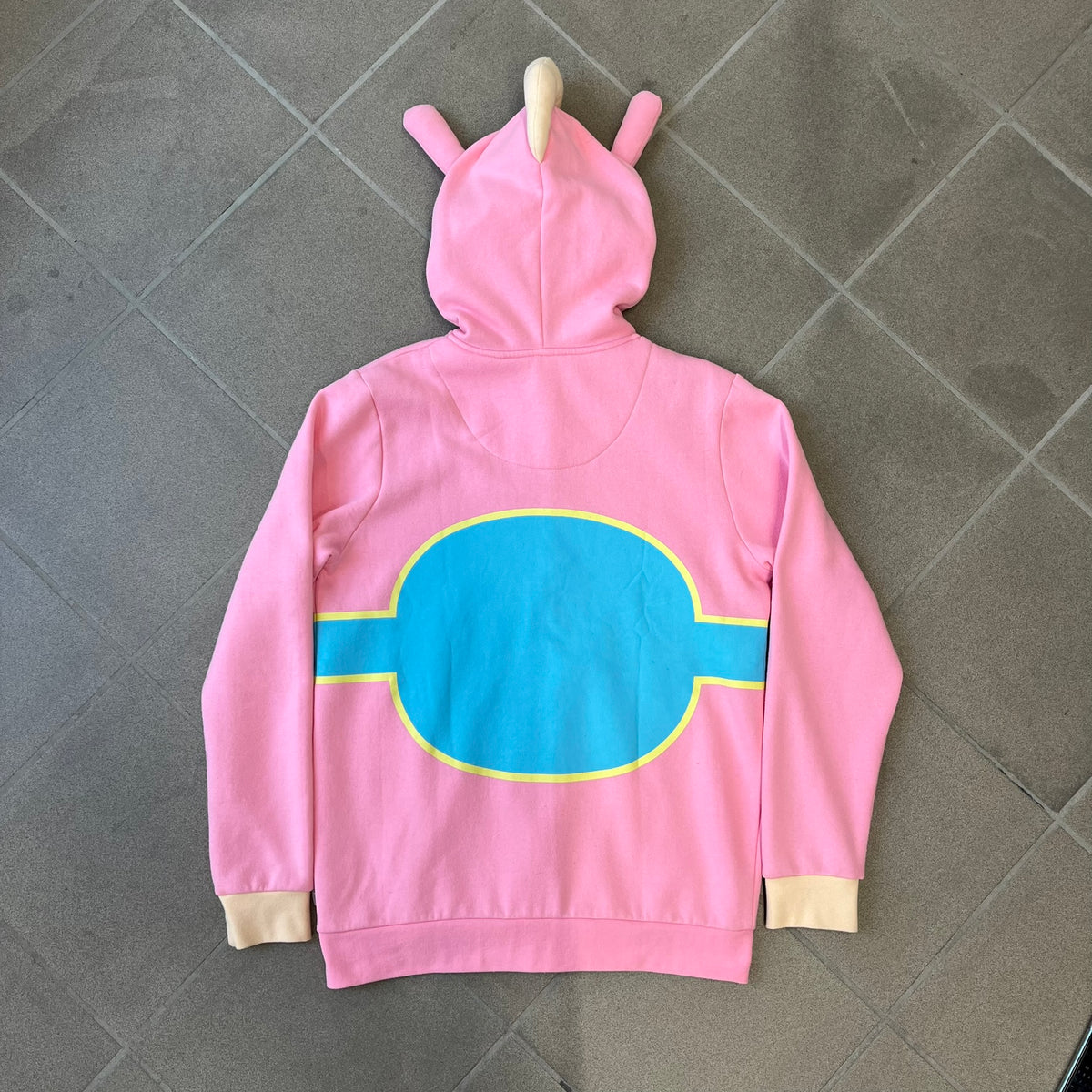 Team Fortress 2 Balloonicorn 2015 WeLoveFine Zip-Up Hoodie is a bright pink unisex colorblock hoodie from Valve’s Team Fortress 2 line, with a detailed 3D plush Balloonicorn hood featuring embroidered eyes, a 3D horn, nose, and ears. It has front pockets, a custom metal Balloonicorn cameo zipper pull, and a light blue printed saddle graphic that wraps from the back to the front. The licensed TF2 neck tag carries 2015 and We Love Fine branding. Super rare.