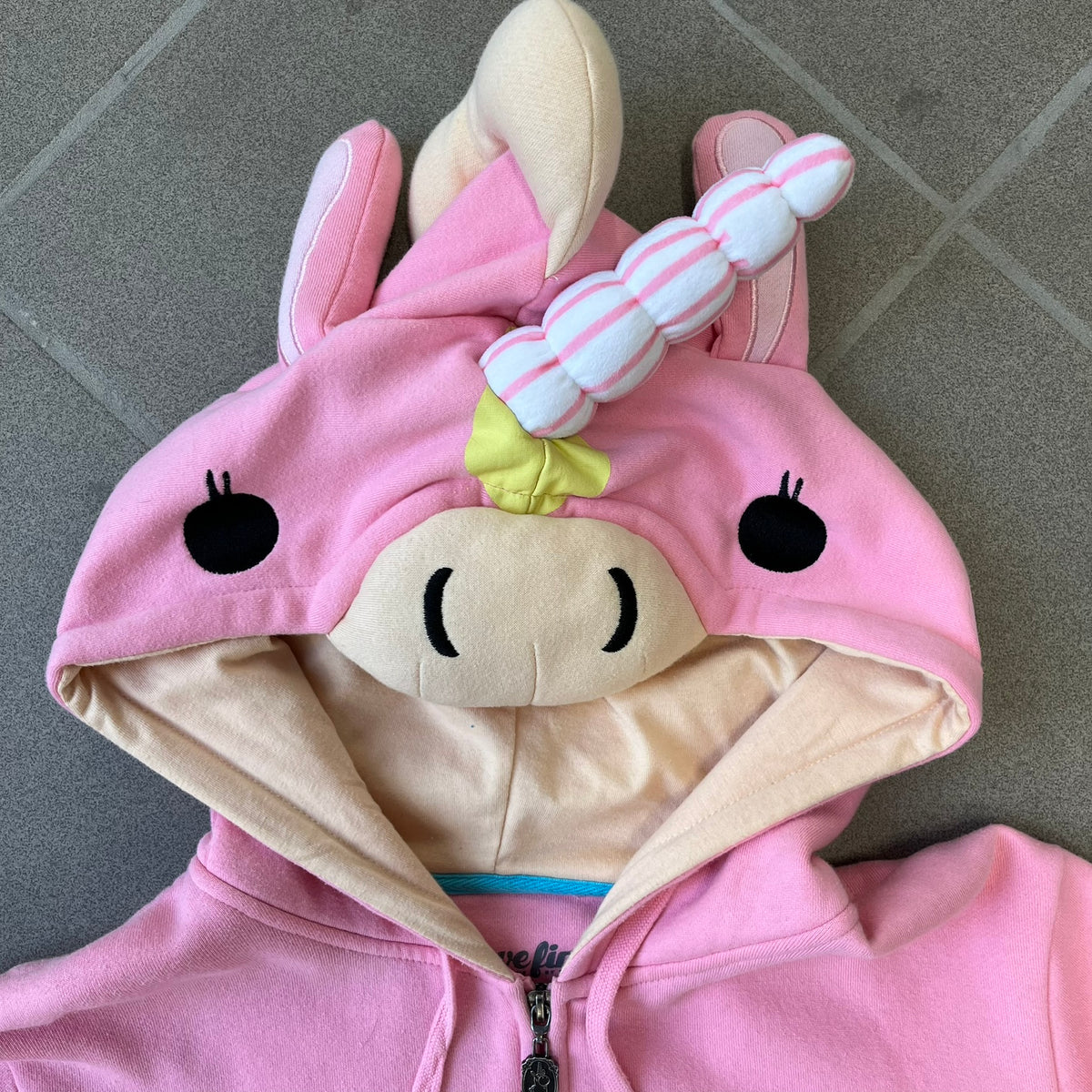 Team Fortress 2 Balloonicorn 2015 WeLoveFine Zip-Up Hoodie is a bright pink unisex colorblock hoodie from Valve’s Team Fortress 2 line, with a detailed 3D plush Balloonicorn hood featuring embroidered eyes, a 3D horn, nose, and ears. It has front pockets, a custom metal Balloonicorn cameo zipper pull, and a light blue printed saddle graphic that wraps from the back to the front. The licensed TF2 neck tag carries 2015 and We Love Fine branding. Super rare.